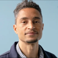 Zach Norris, author of Defund Fear: Safety without Policing, Prisons, and Punishment, stands next to an interior window and gazes at the camera